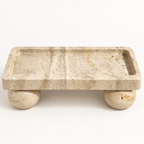 Rectangular beige travertine tray with spherical feet in a studio setting